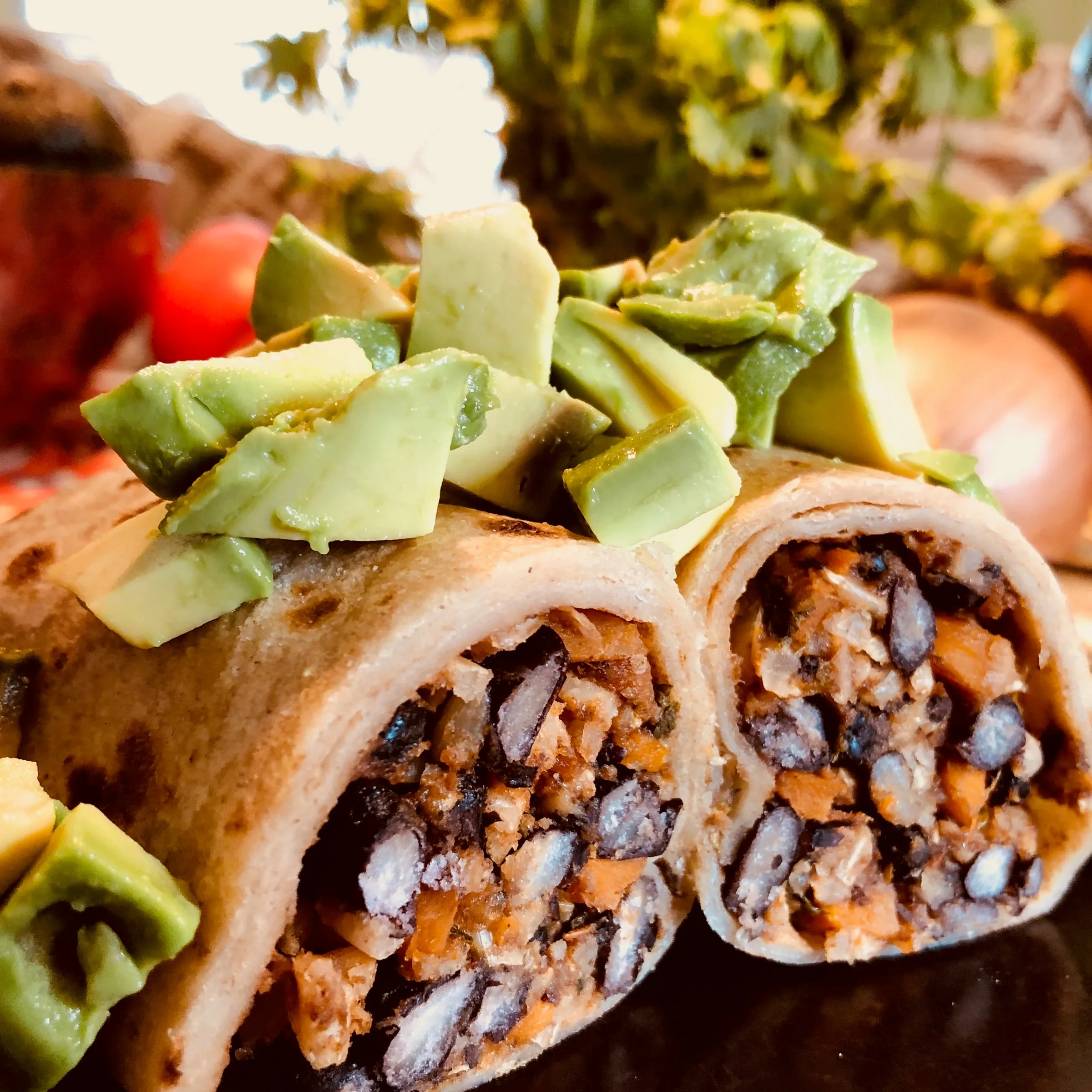 Two halves of a black bean burrito standing upright, topped with diced avocado.