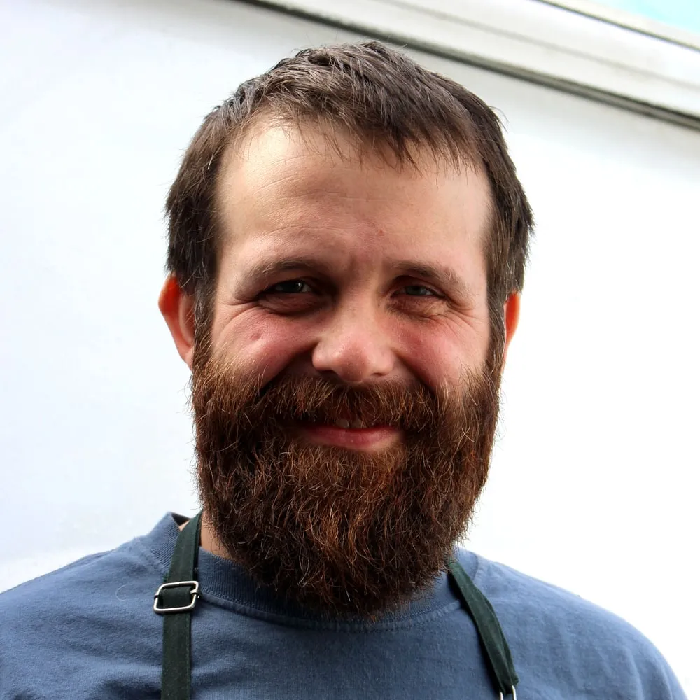 Trey, bearded and in a work apron, smiling in the kitchen doorway.