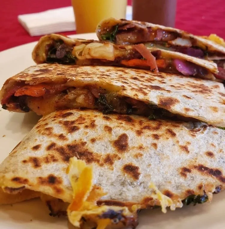 A quesadilla cut into wedges on a white plate, filled with chard, peppers and melted cheese.
