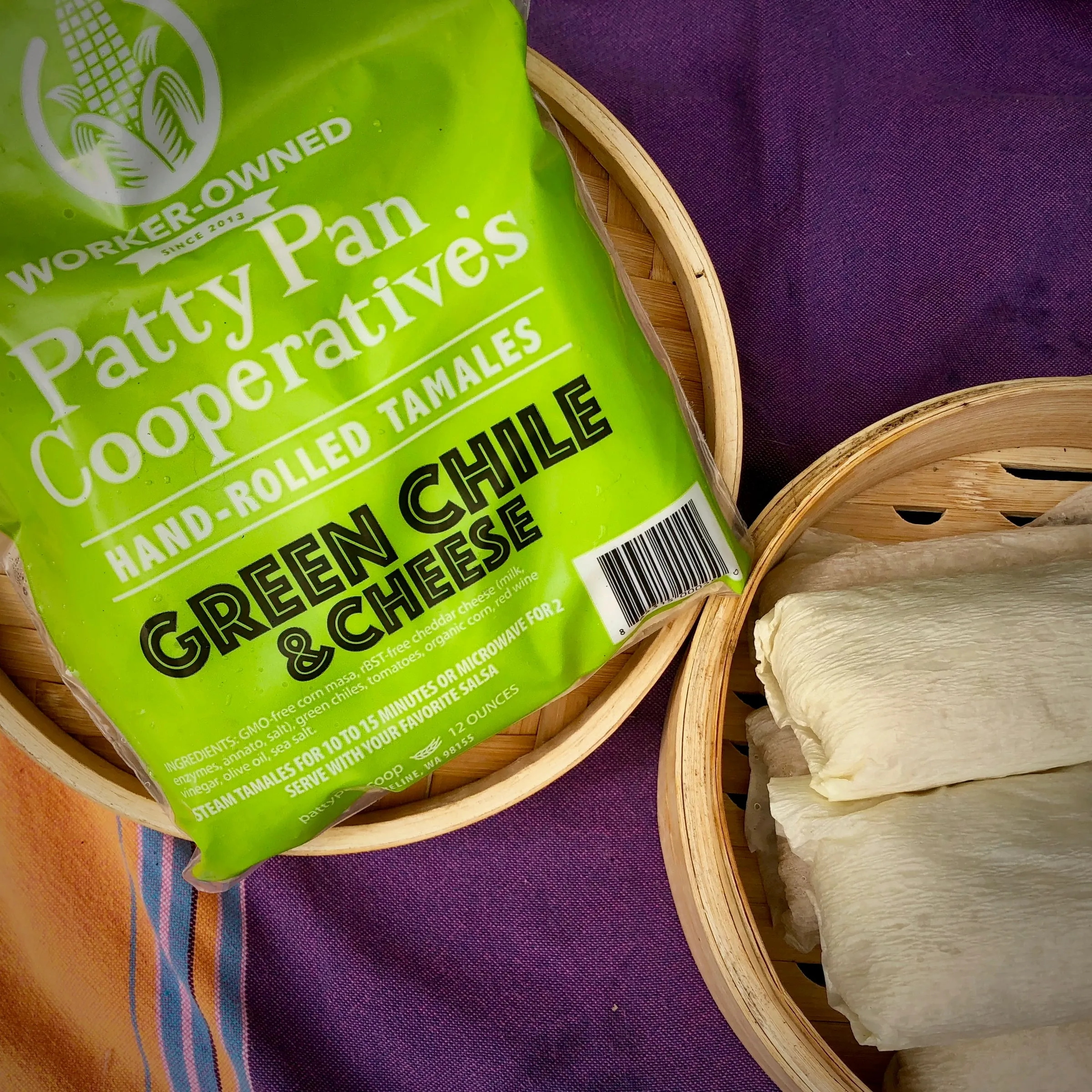 A bag of green chile and cheese tamales beside a bamboo steamer of husk-wrapped tamales.