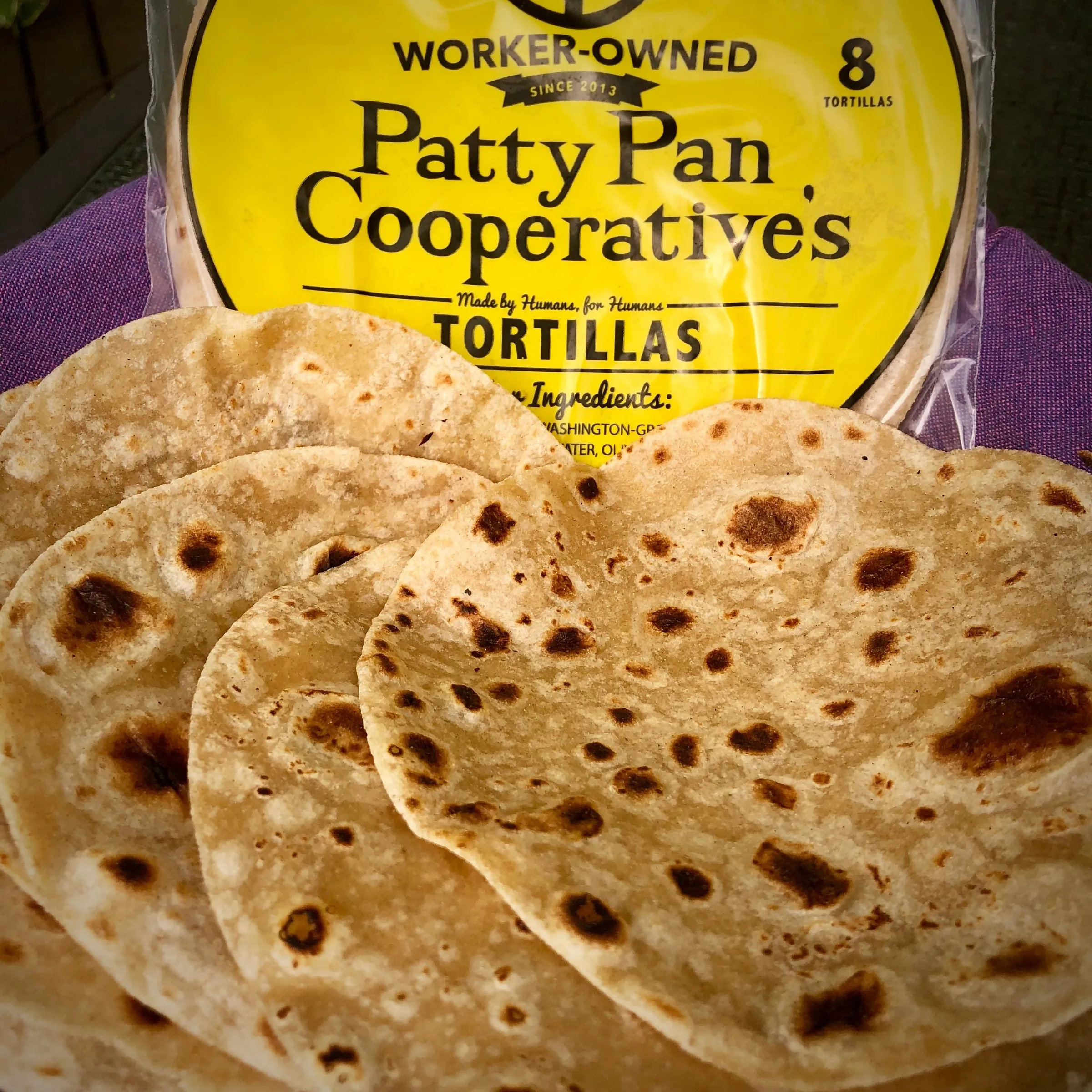 A stack of browned whole wheat tortillas in front of a yellow Patty Pan tortilla package.